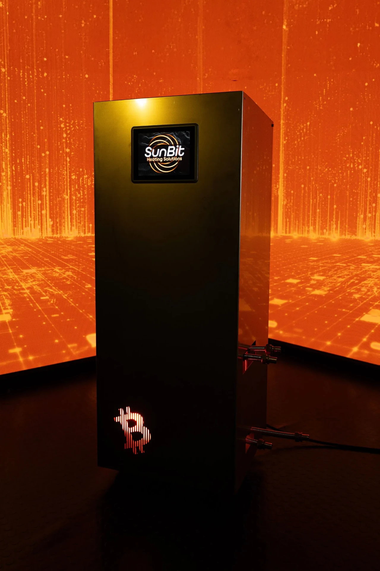 Bitcoin Boiler -lämmitin oranssin hehkun ympäröimänä, kuvaus louhinnan tuottamasta hukkalämmöstä.